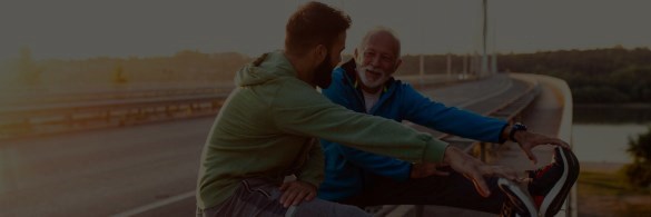 A young and an older man stretching while out running next to a road