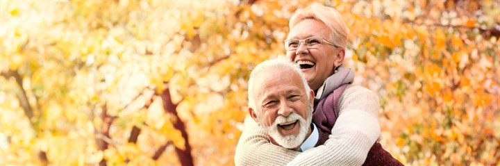 Older couple laughing in front of autumn trees